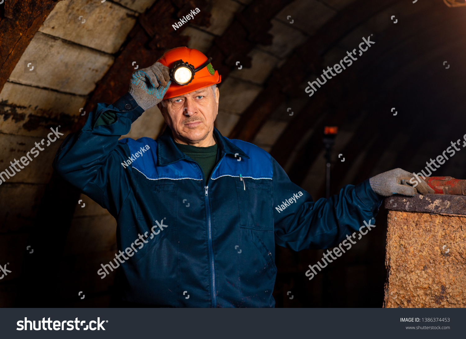 An elderly man dressed in work overalls and a hard hat is standing near the old caravan. Mine worker. Miner #1386374453