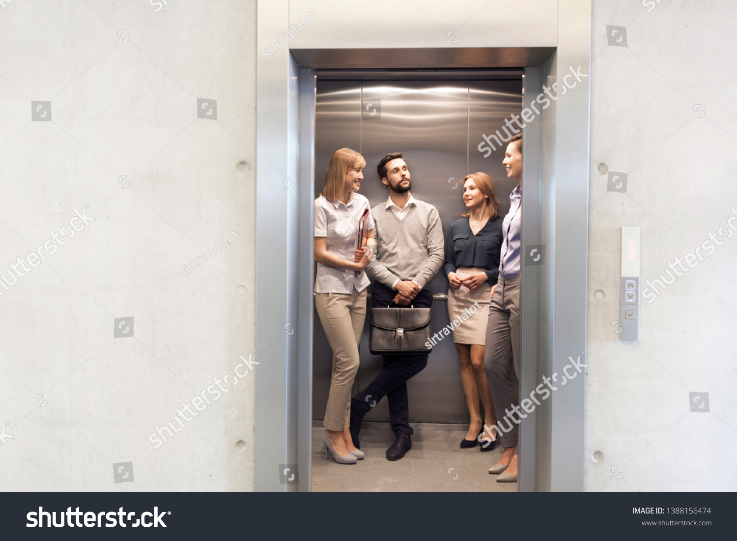 Colleagues talking while standing in elevator at office #1388156474