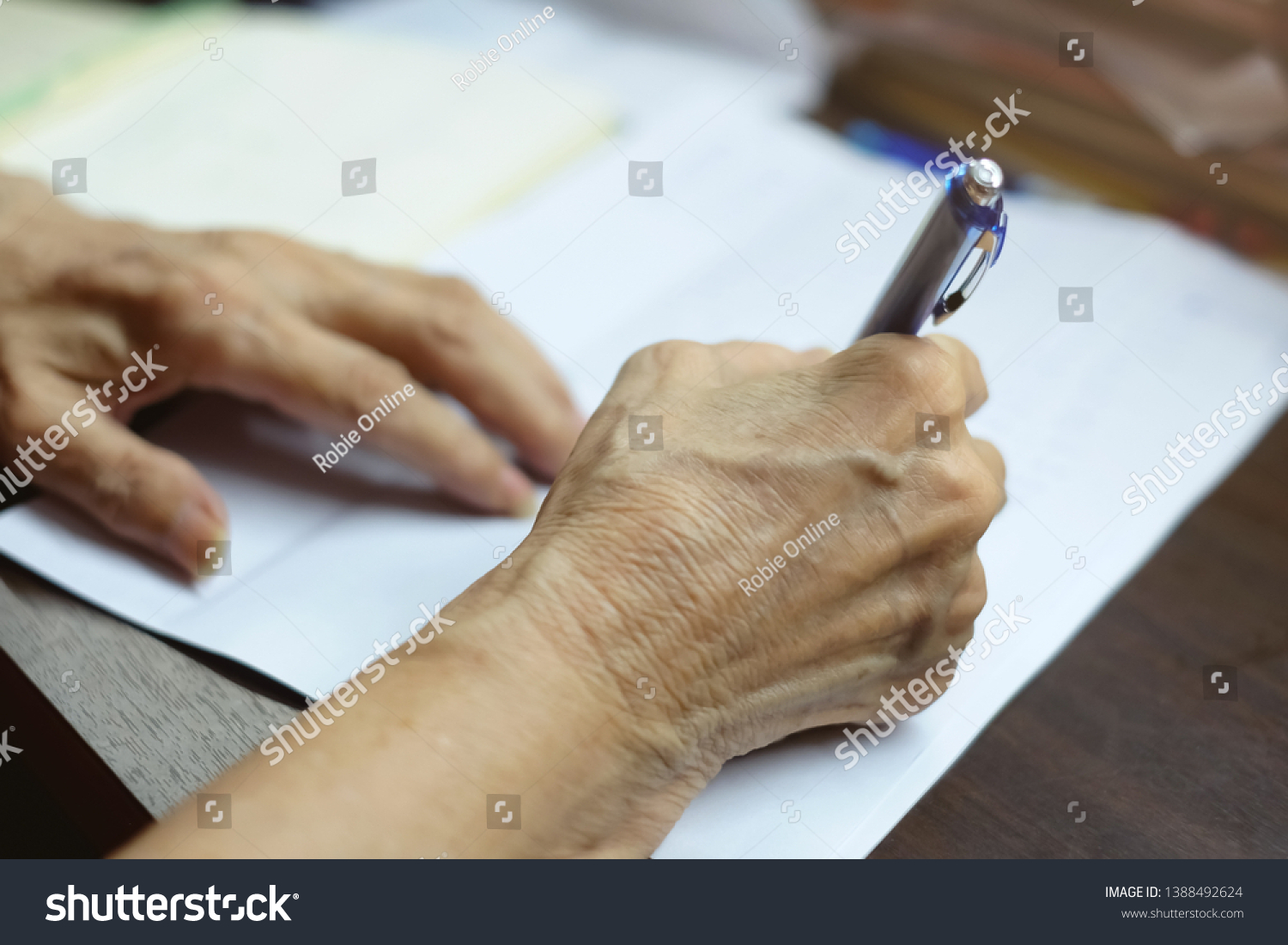 Selective focus at elderly hand using blue pen to writing letter. concept taking note and memorial. Write the letter, Low technology, Send and Receive letter, Retirement, testament signature and law #1388492624