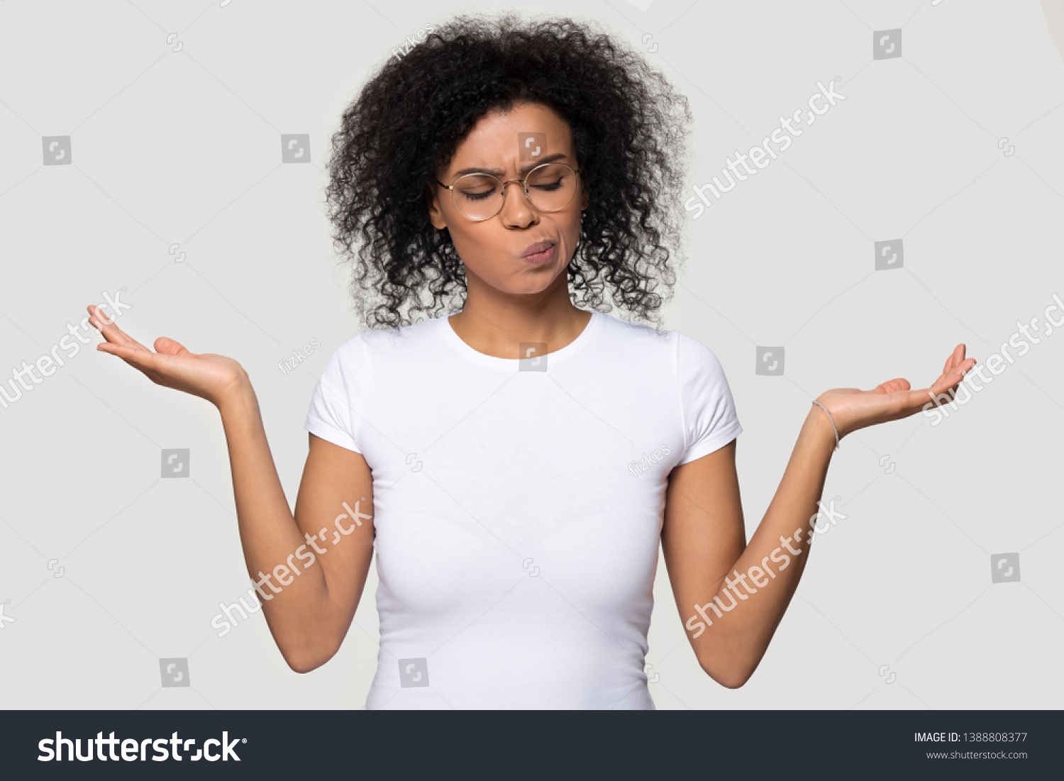 African thoughtful woman in glasses white t-shirt stretched hands imagining alternatives weighs pros and cons isolated on grey blank background, concept of make important decision and choosing option #1388808377