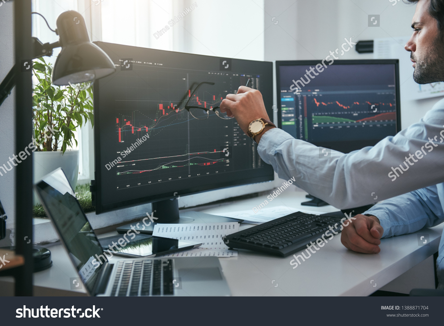 Forex market. Young trader is pointing at graphs on computer screen and analyzing data while working in his modern office. #1388871704