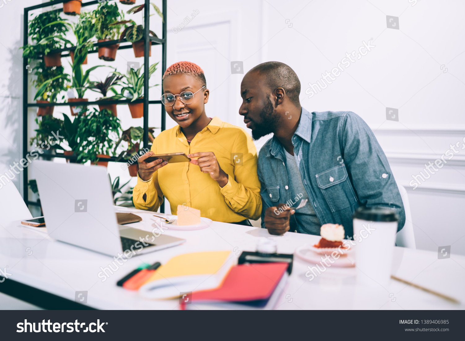 African American guy looking at female colleague taking picture of tasty cafe while eating and working on project in modern cafe together #1389406985