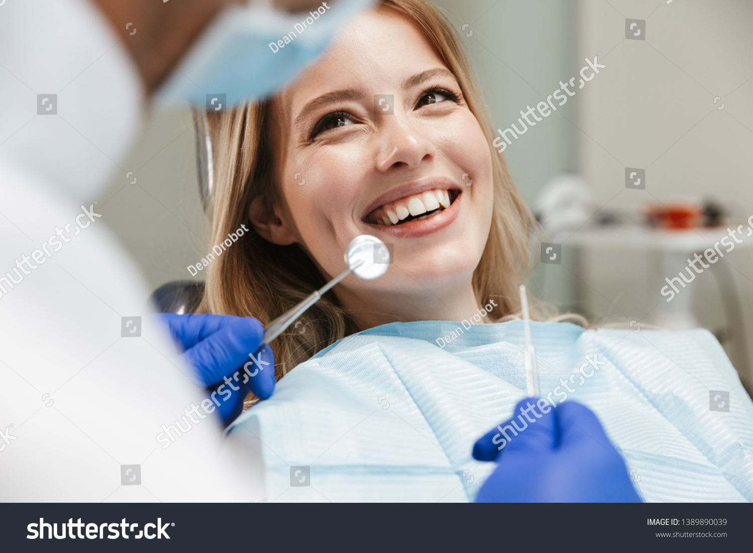 Image of pretty young woman sitting in dental chair at medical center while professional doctor fixing her teeth #1389890039