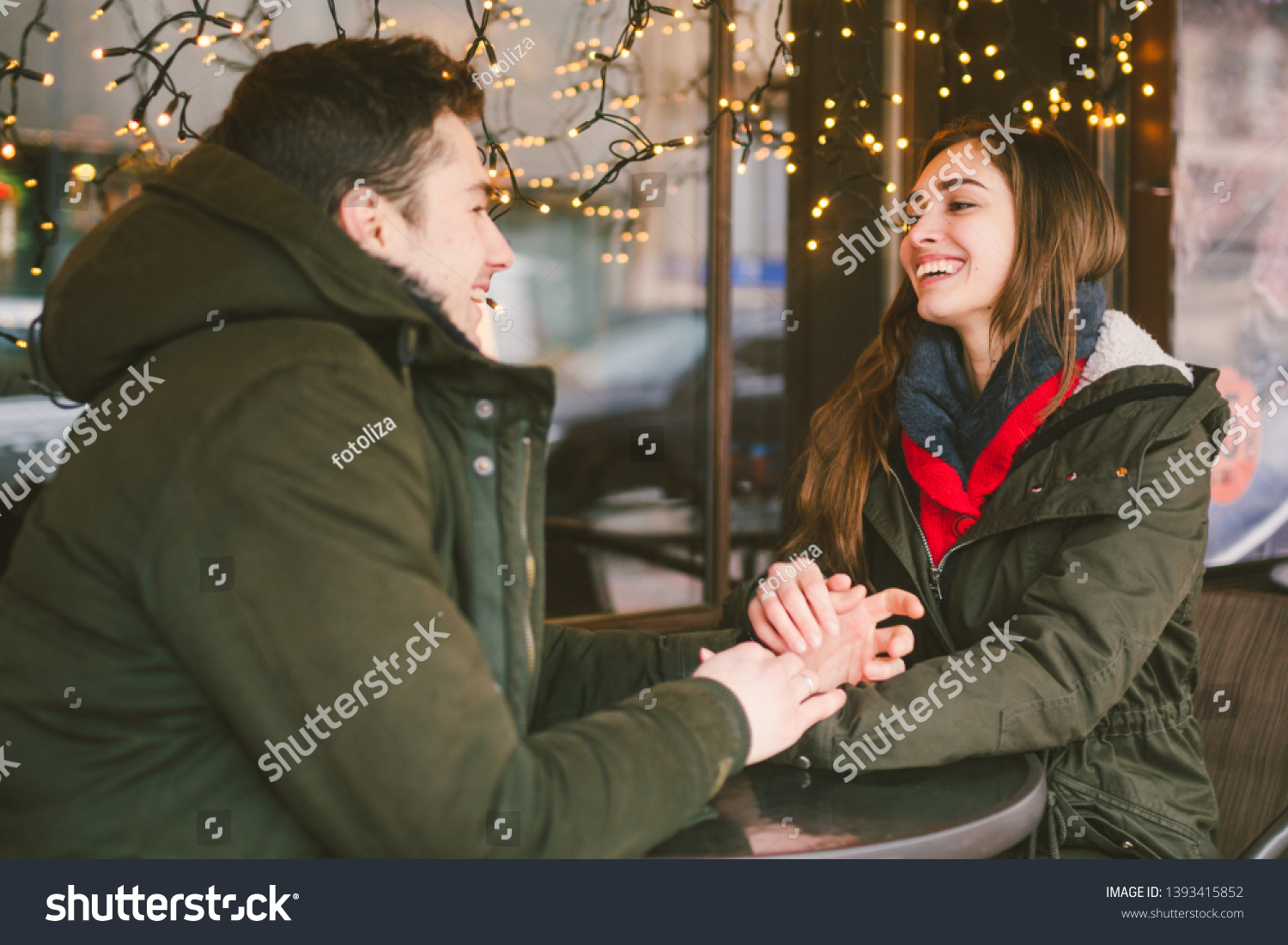 Theme love holiday Valentines Day. pair college students, Caucasian heterosexual lovers in winter, sit table of street cafe against the background window lights. Emotion romance of happiness and love. #1393415852