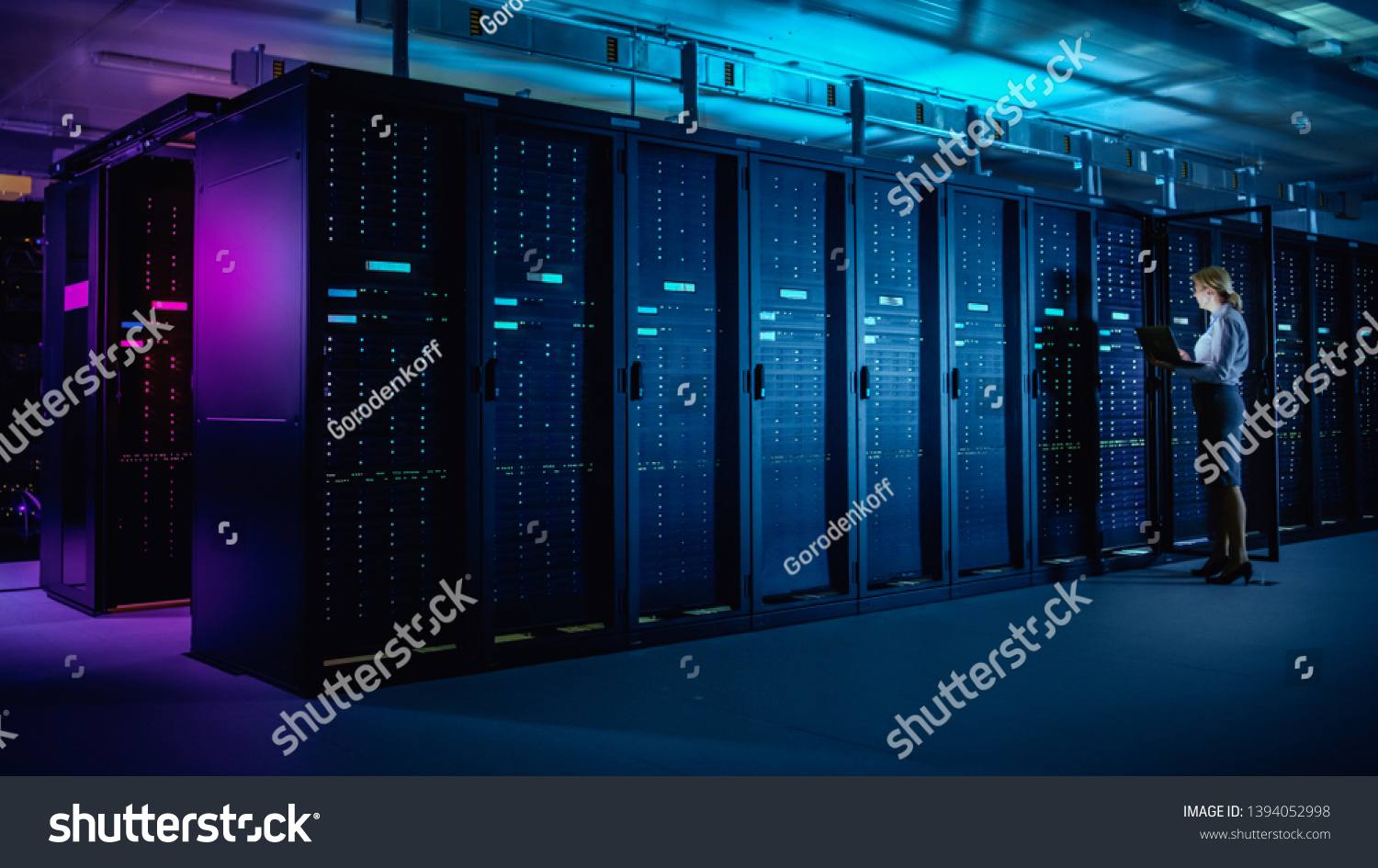In Data Center: IT Technician Running Maintenance Programme on Laptop, Controls Operational Server Rack Optimal Functioning. Modern High-Tech Telecommunications Operational Data Center in Neon Lights. #1394052998