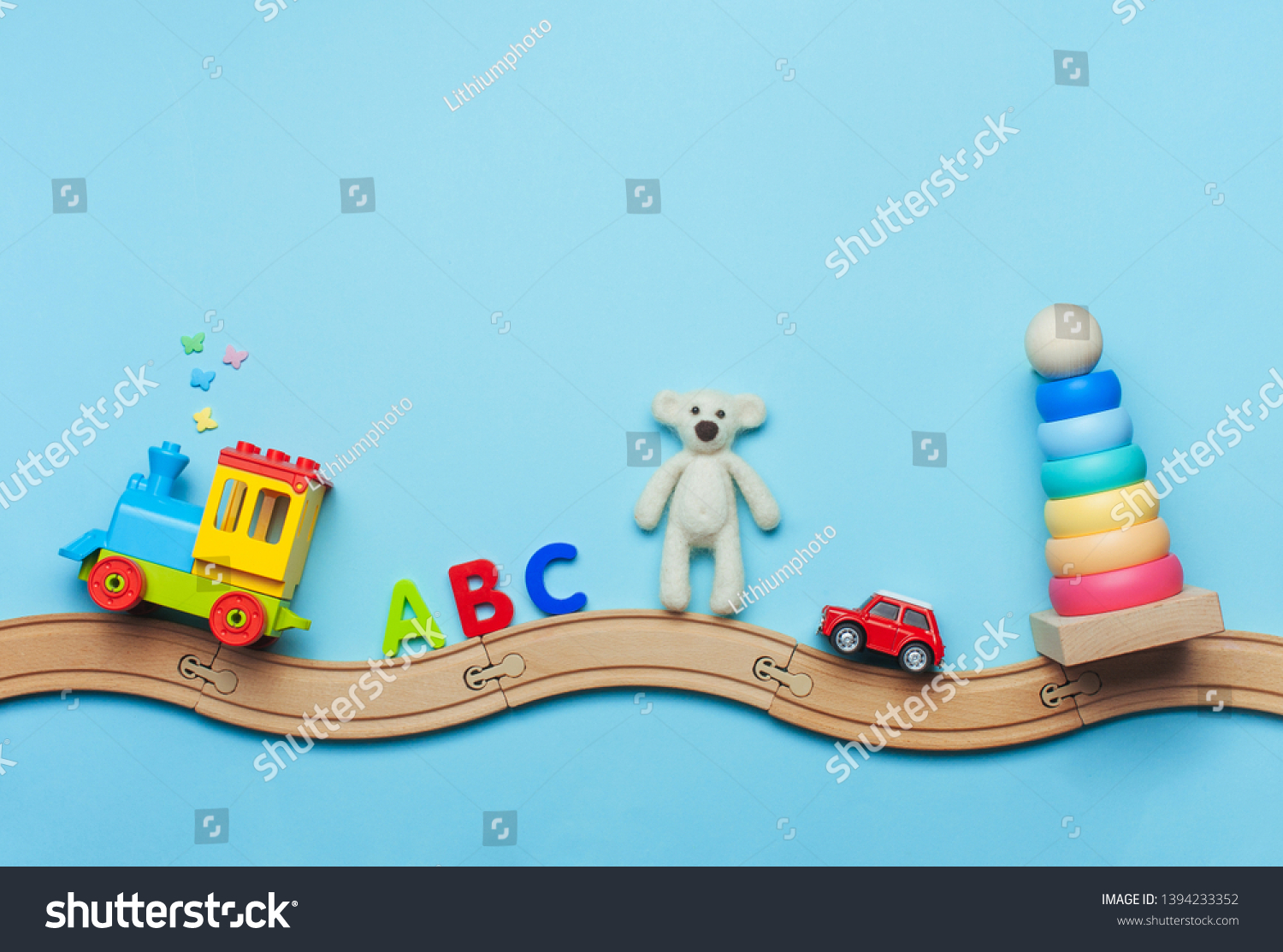 Toys background with copy space. Kids toys train, ABC letters, bear, car and pyramid on toy wooden railway on blue background with blank space for text. Top view, flat lay. #1394233352