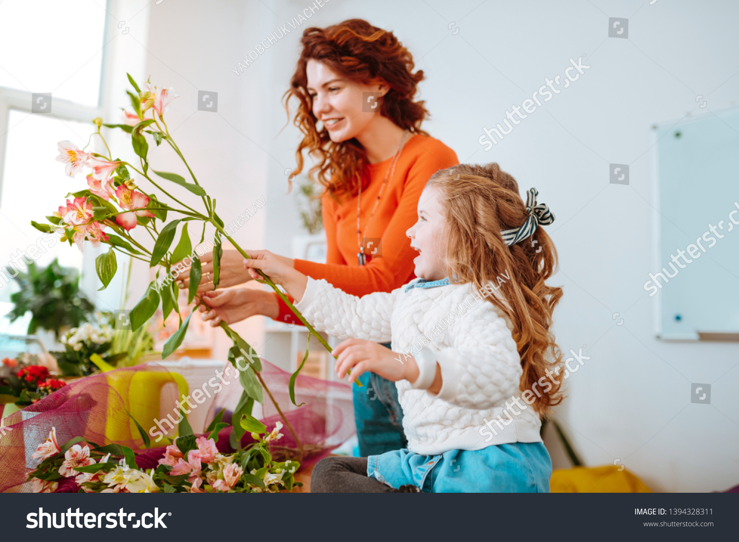 Cheerful daughter. Cheerful daughter with wavy hair having fun while looking at flowers with mom #1394328311