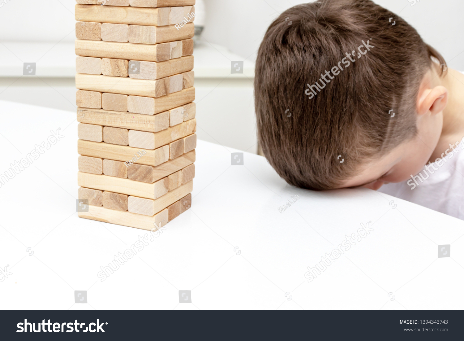 A bored preteen caucasian boy trying to play wooden block tower board game to entertain himself. #1394343743