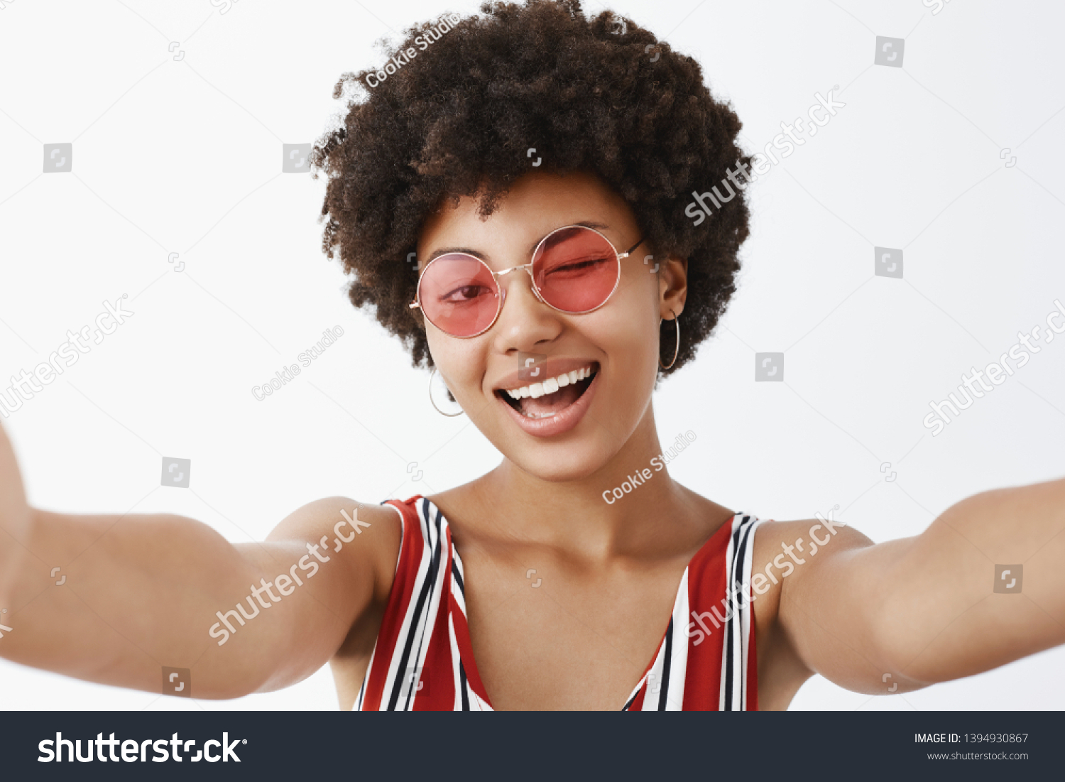 Hey, what is up. Playful hot African American with afro hairstyle, pulling hands towards camera to make selfie, winking joyfully and smiling broadly, making new profile pic for social network #1394930867