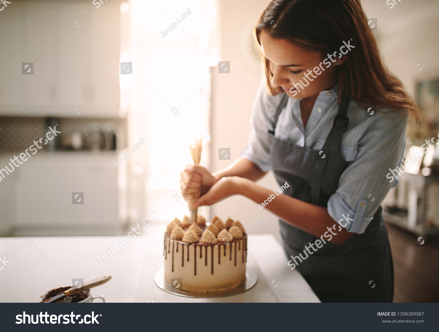 Woman decorating chocolate cake in the kitchen. Female chef making a cake at home. #1398389987