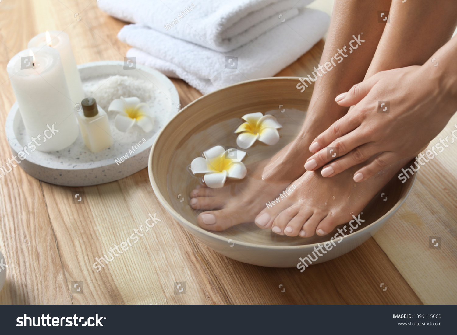 Closeup view of woman soaking her feet in dish with water and flowers on wooden floor. Spa treatment #1399115060