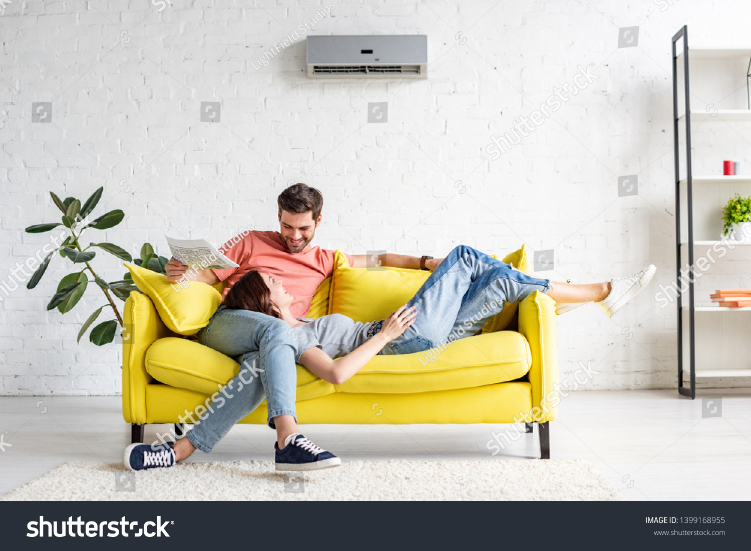 happy man with smiling girlfriend relaxing on yellow sofa under air conditioner at home #1399168955