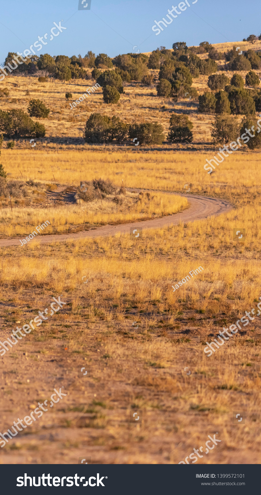 Vertical Unpaved trail winding through a vast grassy terrain viewed on a sunny day #1399572101