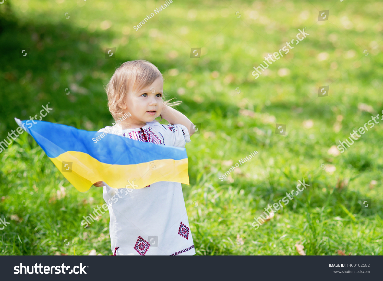 Child carries fluttering blue and yellow flag of Ukraine in field. Ukraine's Independence Day. Flag Day. Constitution day. Girl in traditional embroidery with flag of Ukraine #1400102582