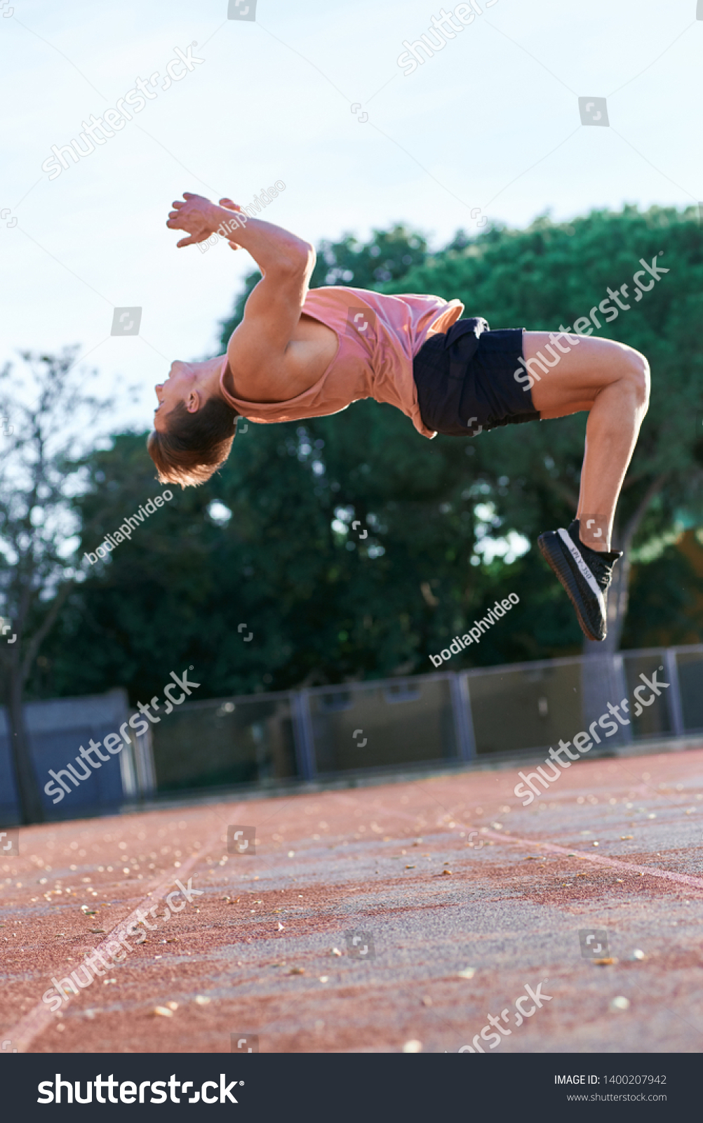 A young boy leaping somersault on the stadium. Copy space. Man athlete doing exercises outdoors. #1400207942