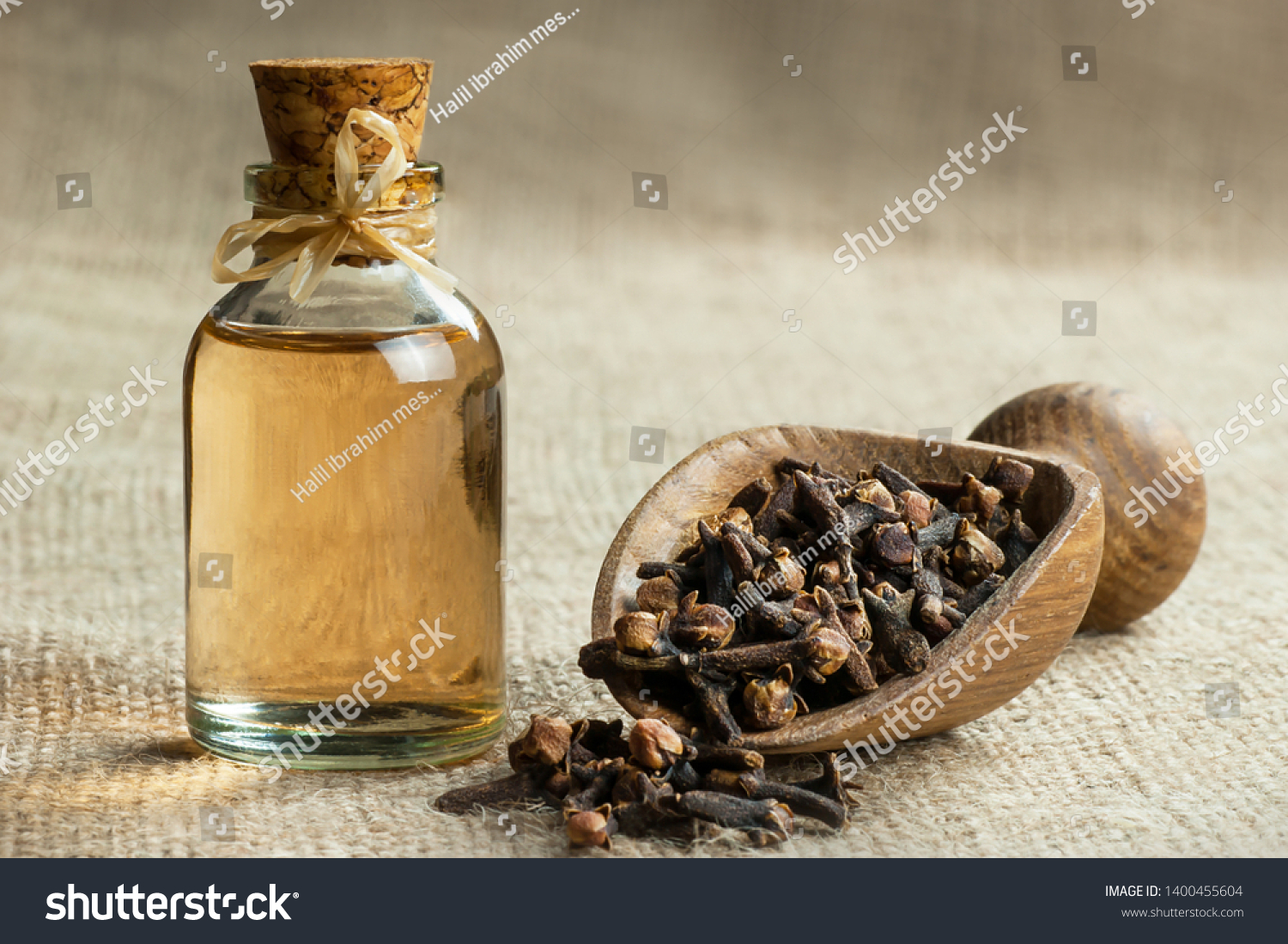 Close up glass bottle of clove oil and cloves in wooden shovel on burlap sack. Essential oil of clove rustic style background spice concept  #1400455604