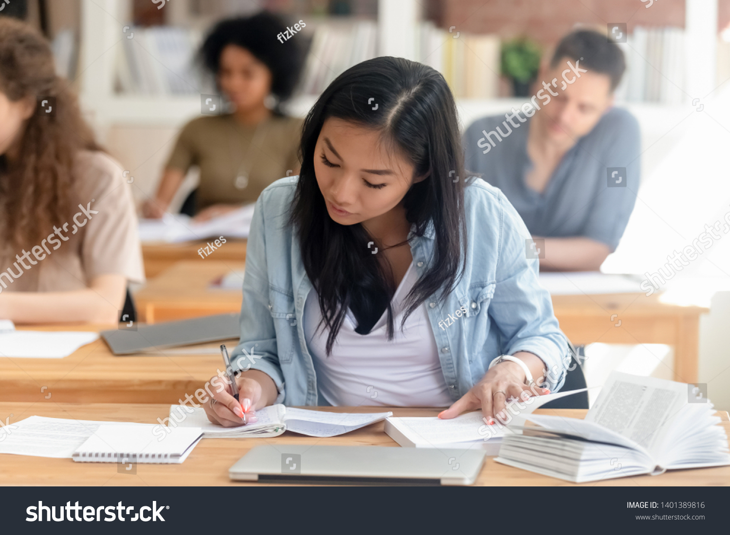 Focused millennial Asian female student sit in shared coworking space studying with handbook writing do homework, concentrated teen girl make notes in workbook prepare for test or exam in library #1401389816