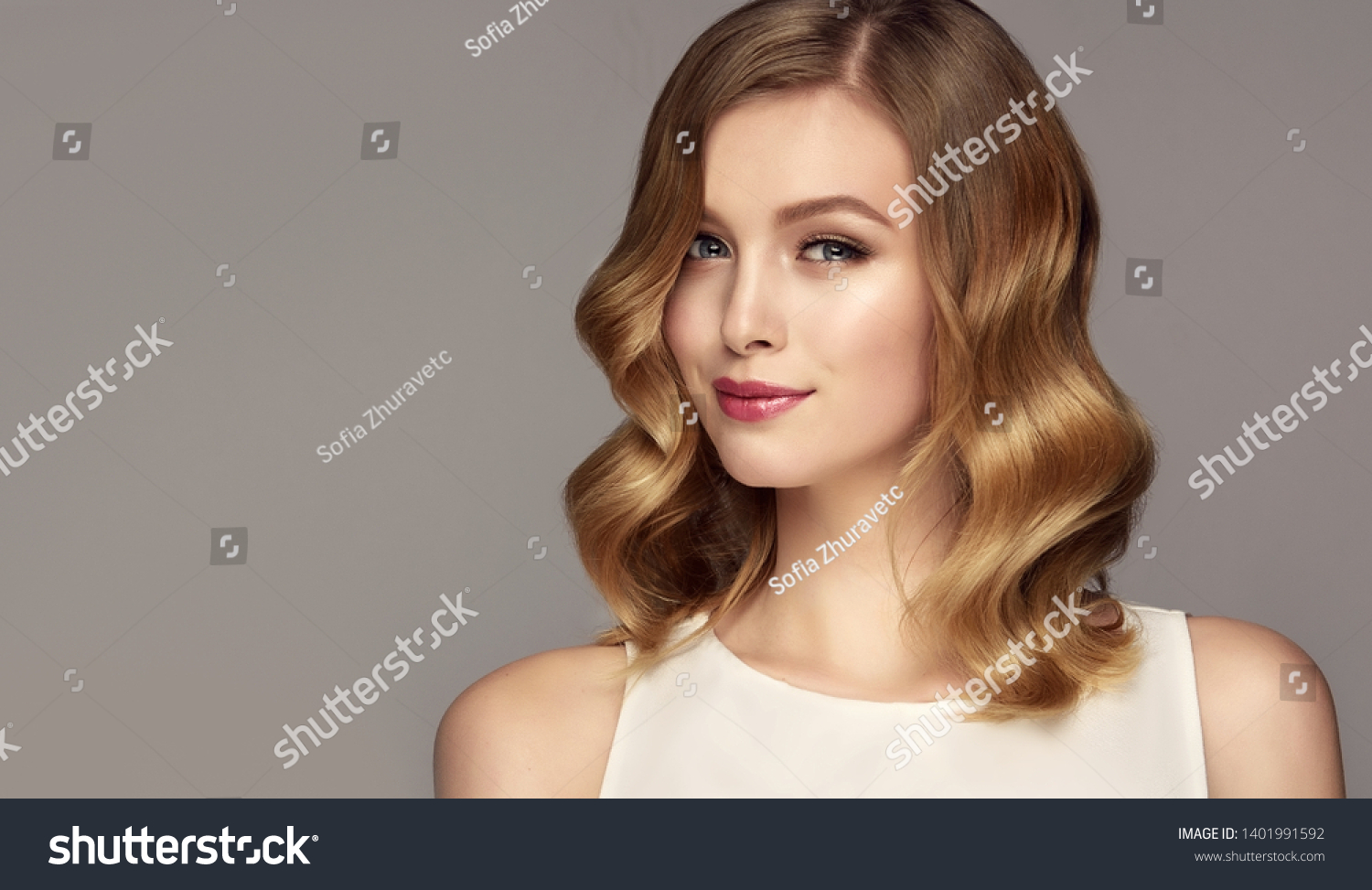 Blonde woman with curly beautiful hair  on gray background. The girl with a pleasant smile. Short haircut . Bob hairstyle
 #1401991592