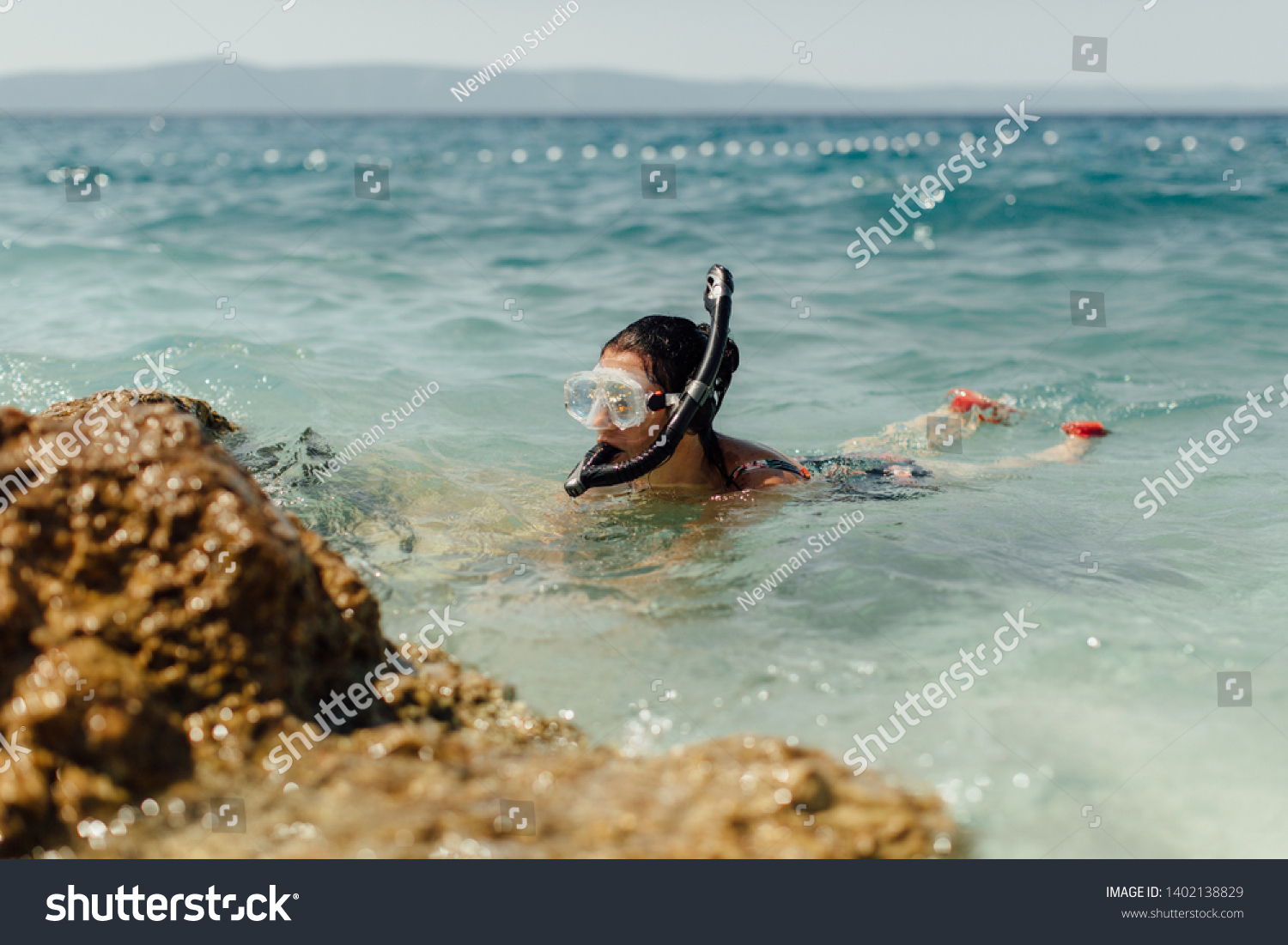 Female diver learning to dive at seashore. Woman wearing diving mask and snorkel snorkeling in sea on hot sunny day. #1402138829