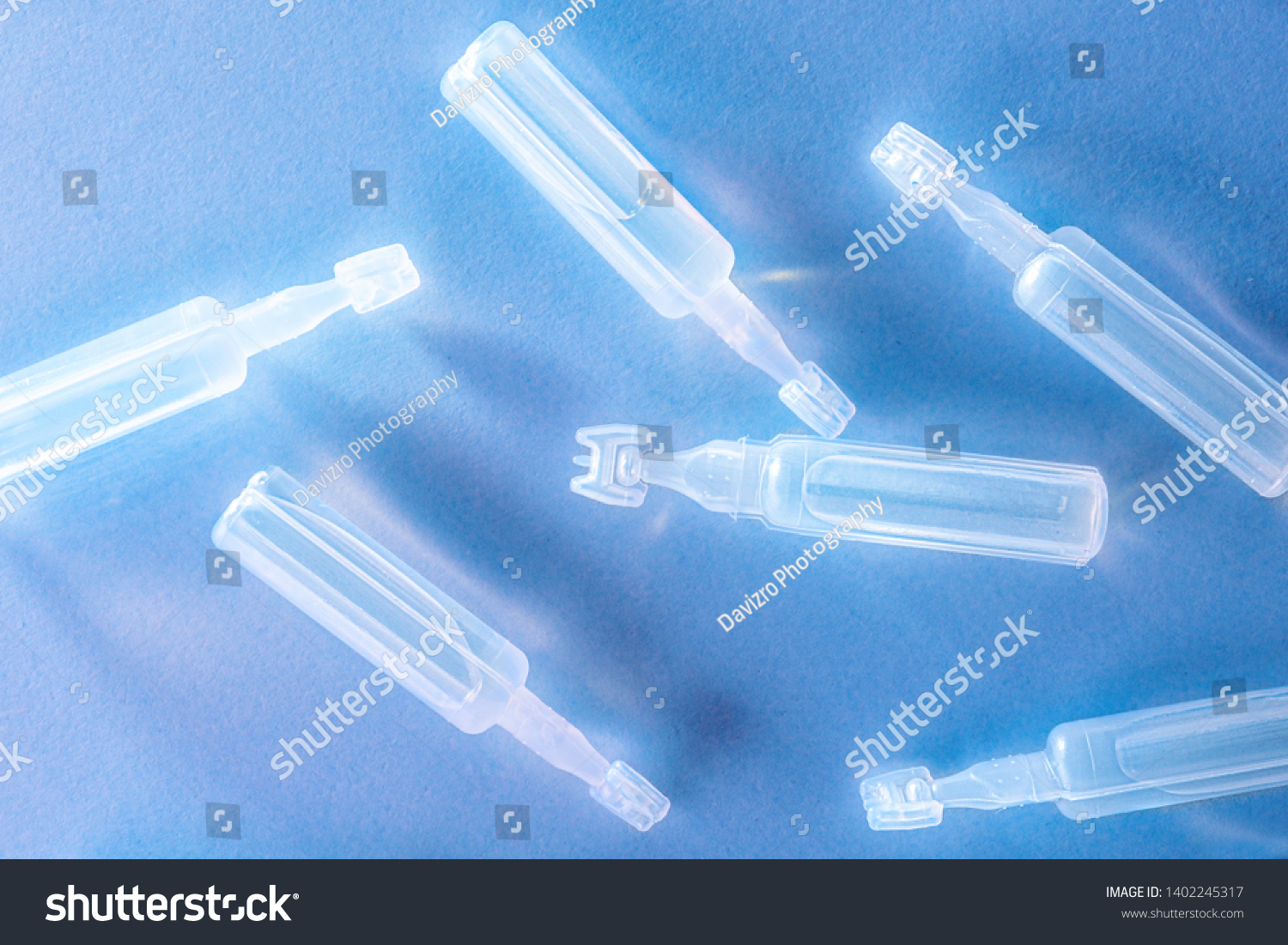 Artificial tears eye drops encapsulated in plastic pipettes and reflected on glass table with blue background. Horizontal composition. Top view. #1402245317