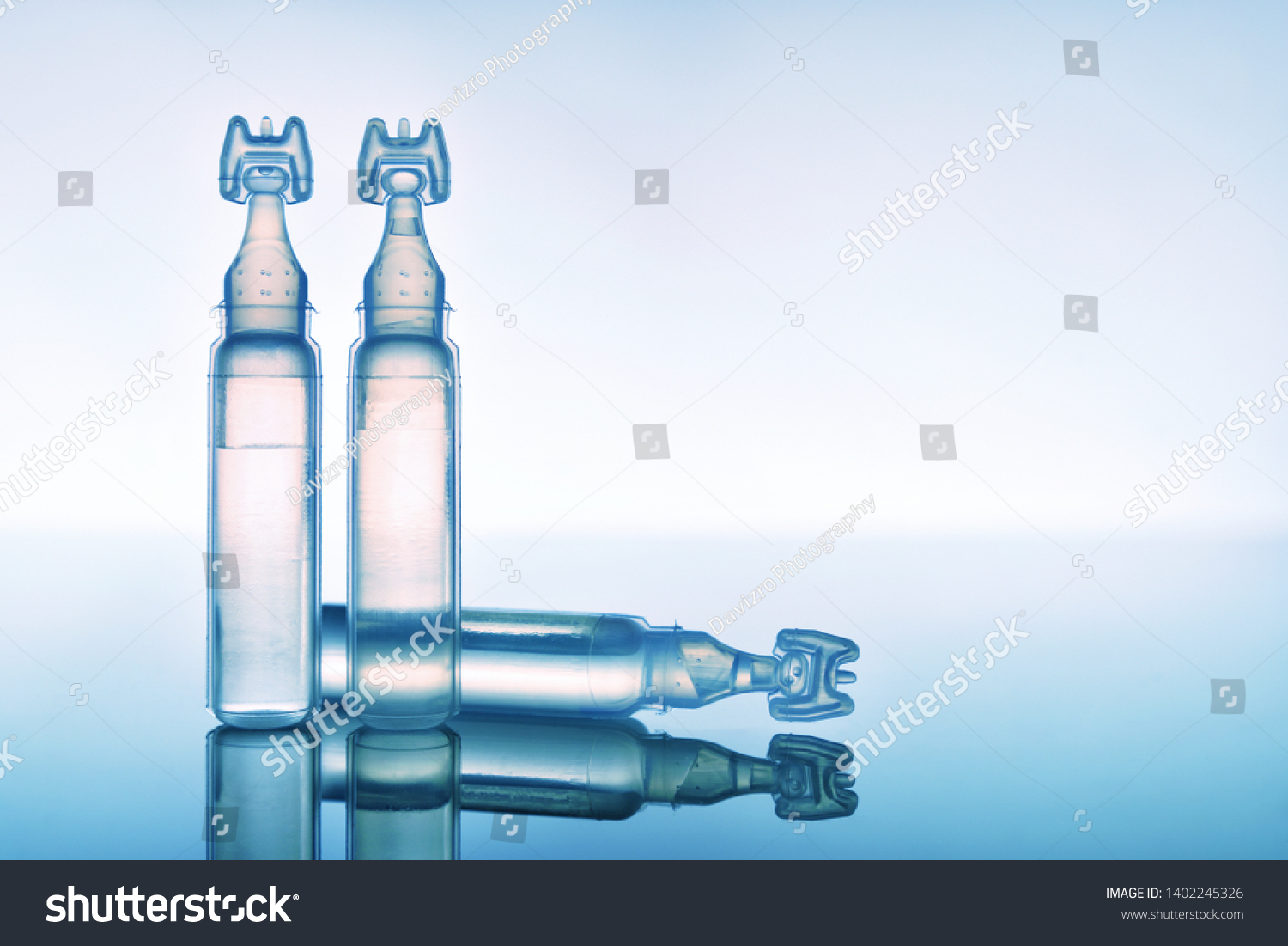 Artificial tears eye drops encapsulated in plastic pipettes and reflected on glass table with blue background. Horizontal composition. Front view #1402245326