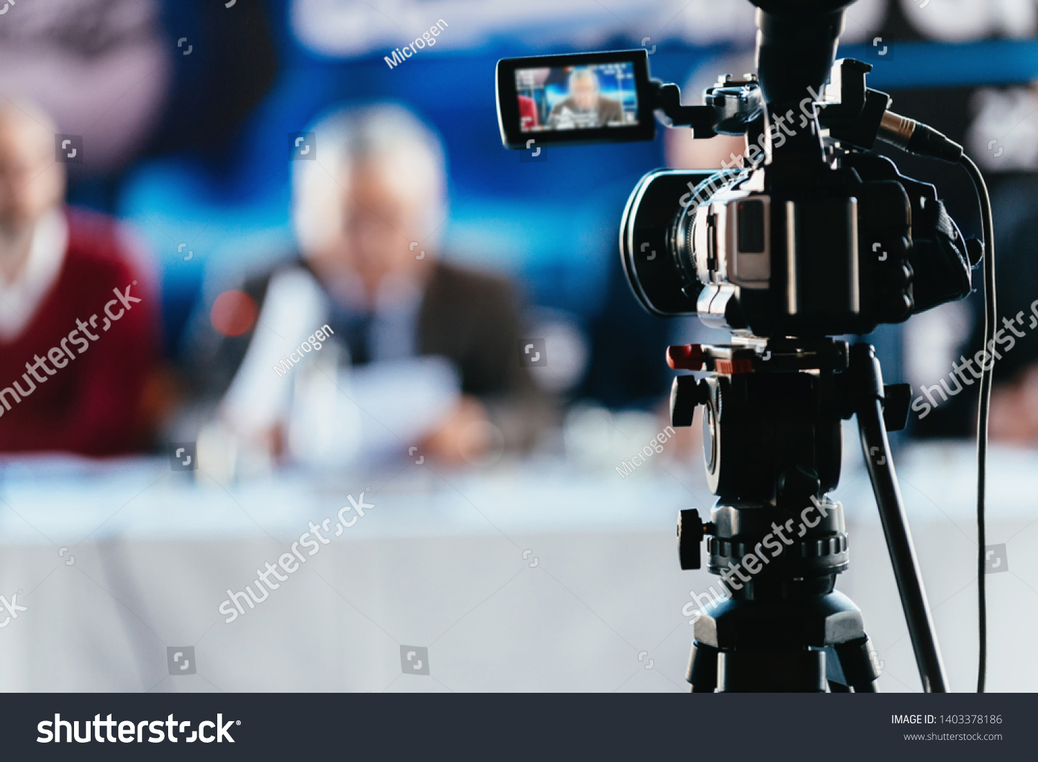 Professional digital camera recording presentation of a blurred speaker wearing suit, live streaming concept #1403378186