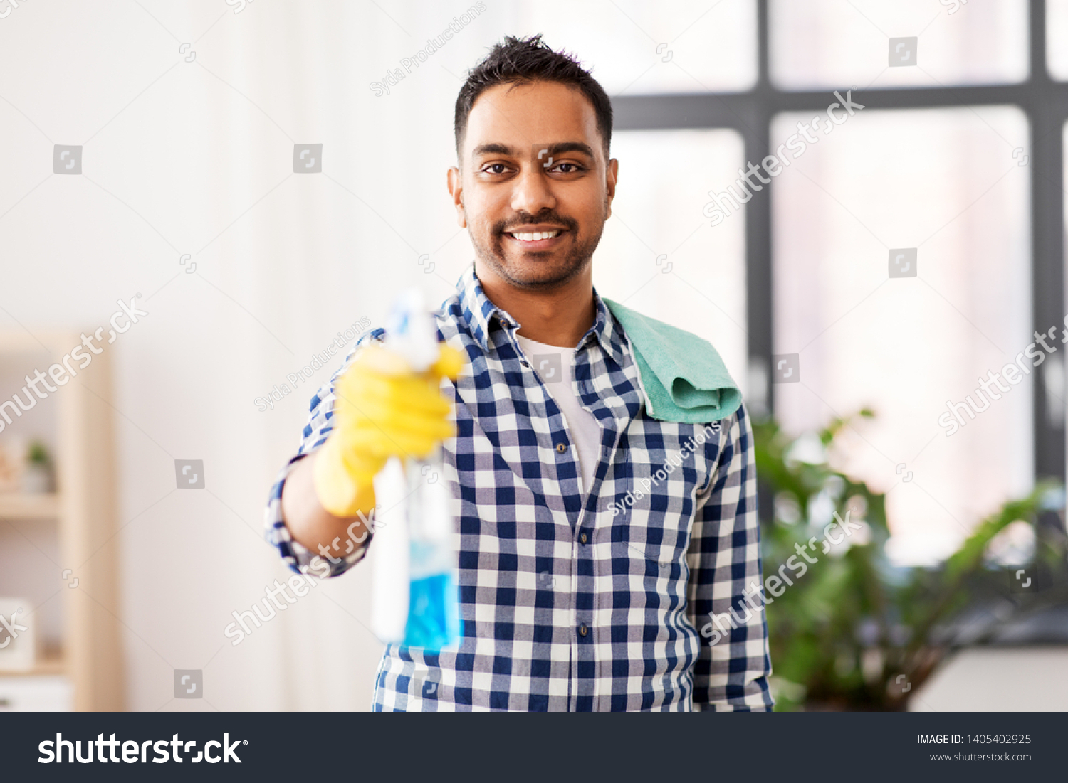 cleaning, housework and housekeeping concept - smiling indian man with detergent and rag on shoulder at home #1405402925
