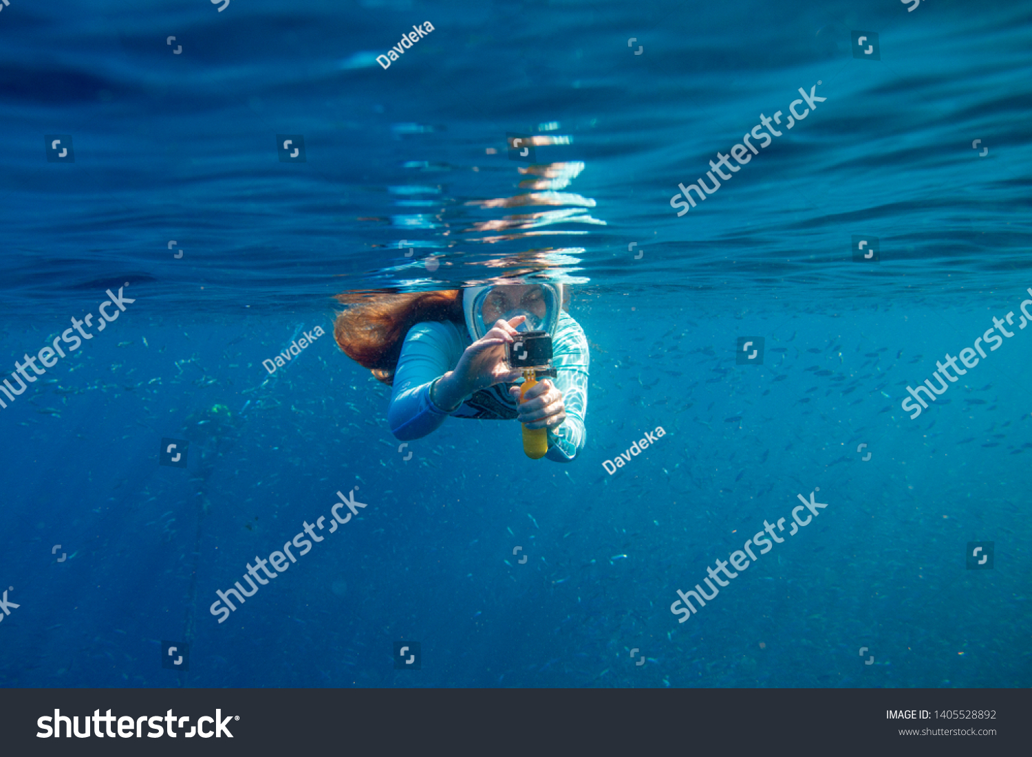 Woman making photo underwater. Girl snorkeling in full-face mask. Snorkel with fish under water surface. Snorkeling gear. Action camera. Active vacation by tropical seaside. Diving girl in open water #1405528892
