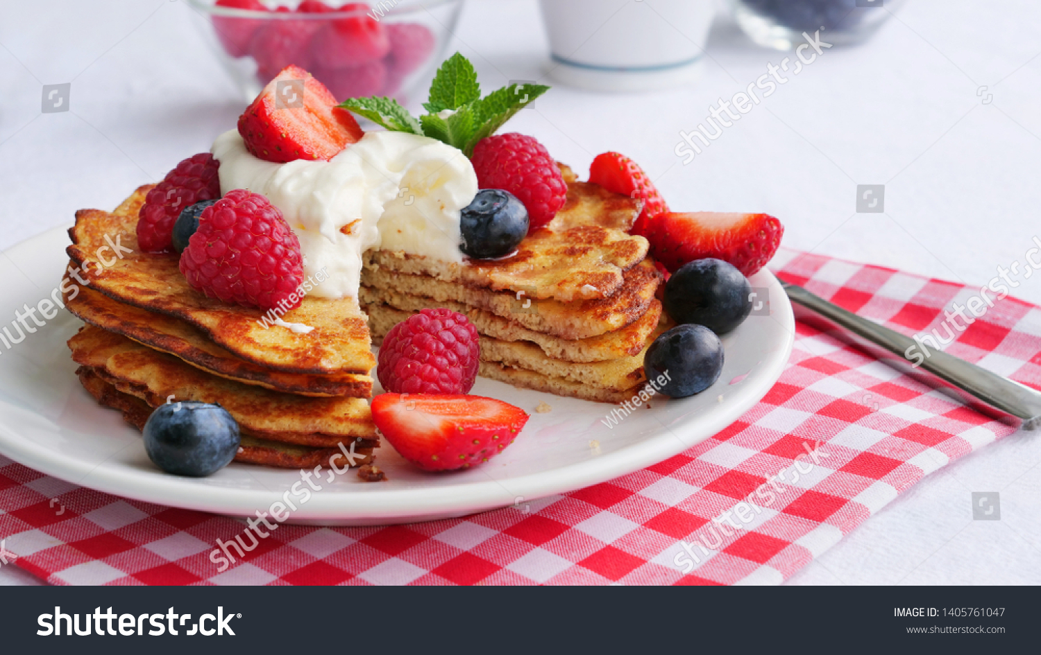 Stack of keto pancakes made of coconut flour or almond flour, served with berries and whipped cream on plate. One slice eaten already. #1405761047