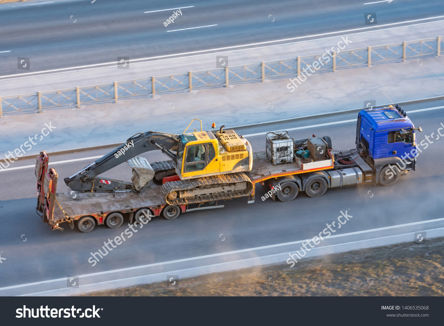 Truck with a long trailer platform for transporting heavy machinery, loaded crawler excavator with bucket. Highway transportation #1406535068