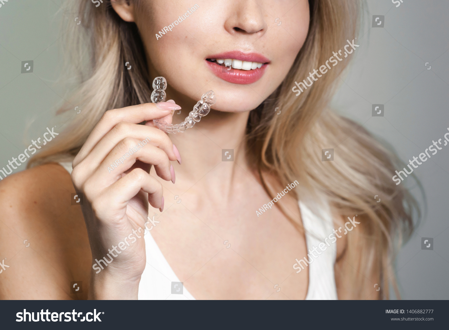 A smiling woman holding invisalign or invisible braces, orthodontic equipment. Teeth aligner for young girl. Dentistry beautiful smile concept #1406882777