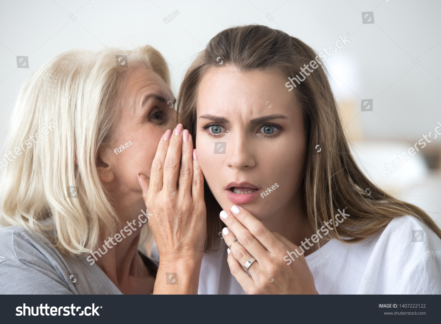 Close up portrait attractive middle aged woman whispering gossiping to ear a secret to millennial female sitting together at home. Best friends trusting relations between mother and daughter concept #1407222122