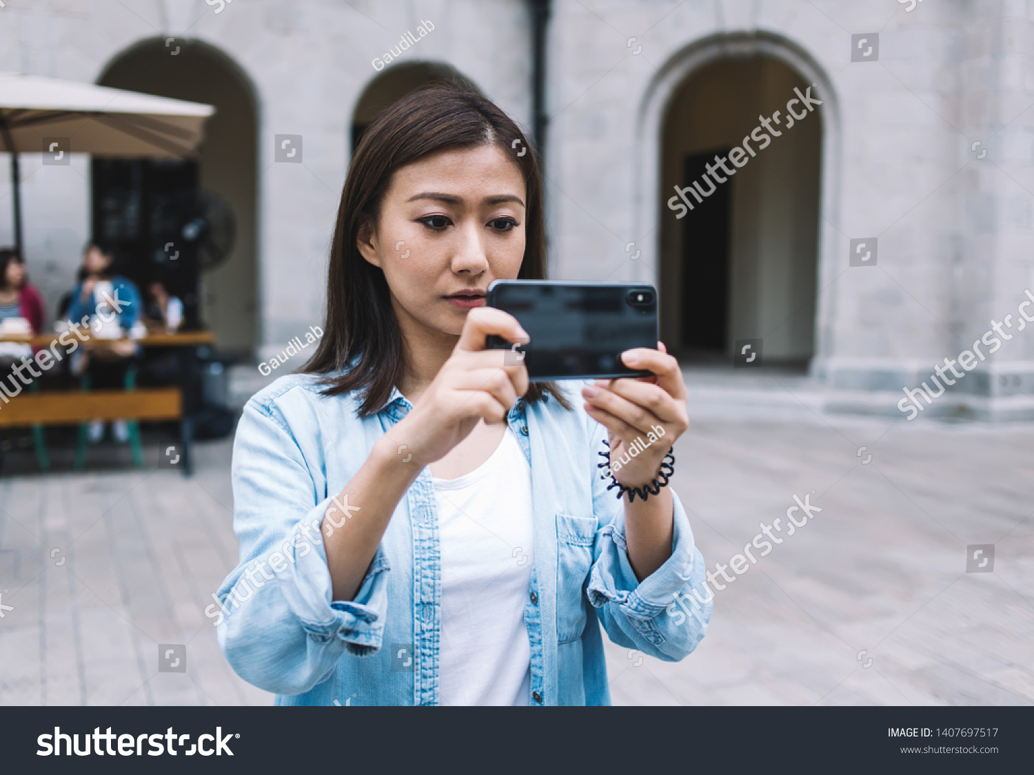 Attractive tourist taking pictures and shooting video on mobile phone for publication in internet networks via 4G internet standing in historic center with public wifi, Asian woman clicking images #1407697517