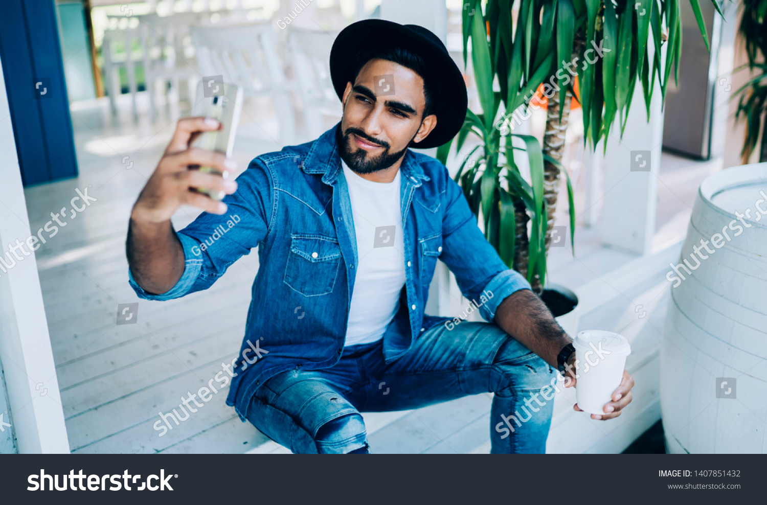 Handsome millennial guy holding takeaway cup with caffeine beverage and clicking selfie pictures, Turkish male blogger photographing himself for creating content publication on fashion web page #1407851432