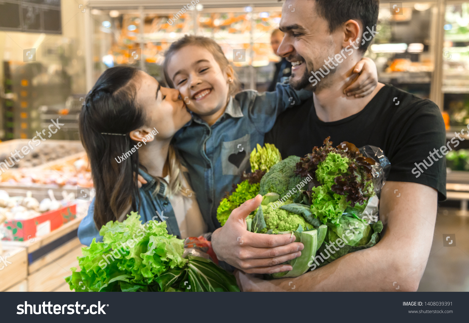 Happy husband and wife with a kid buys vegetables. Cheerful family of three choosing bell pepper and greens in vegetable department of supermarket or market. #1408039391