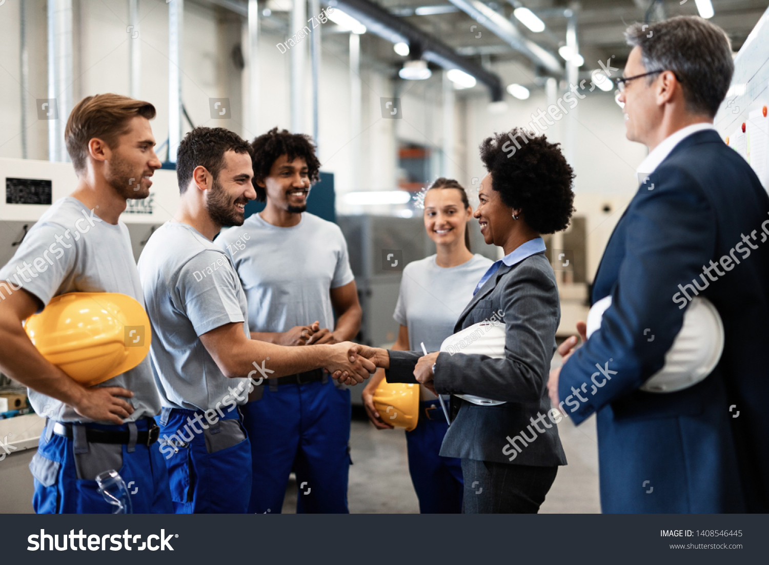 Happy manual worker handshaking with African American manager who is visiting factory with her colleague.  #1408546445