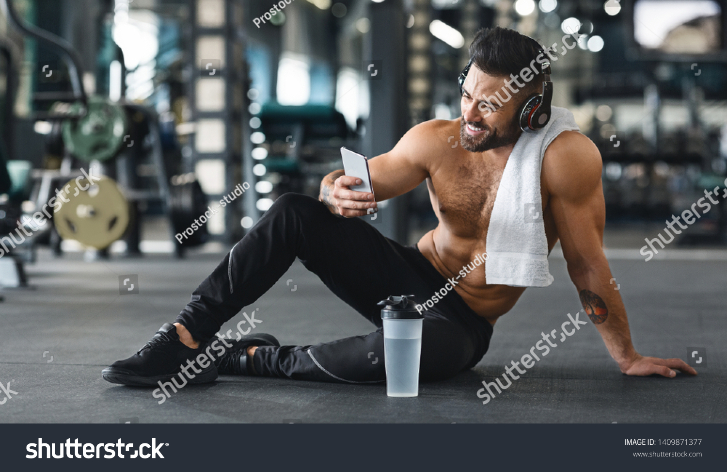 Online personal trainer on mobile phone. Muscular man using cellphone at gym, free space #1409871377