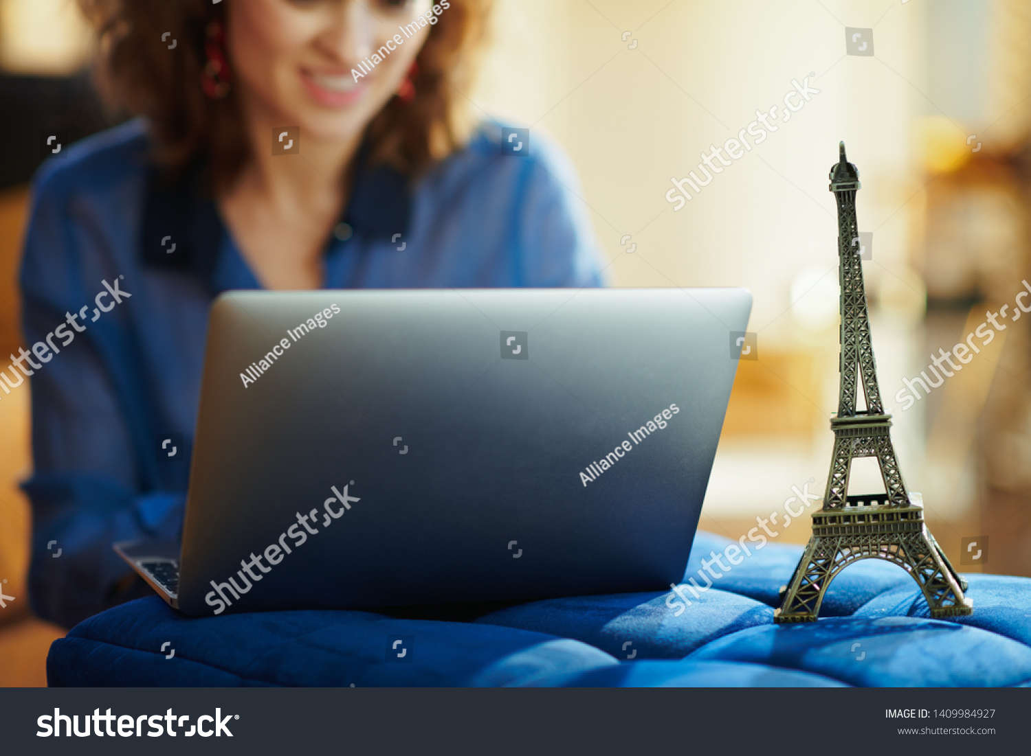 Closeup on a souvenir of the eiffel tower and woman with laptop in background at modern home in sunny summer day. A fake website is made for illustrative purposes. #1409984927