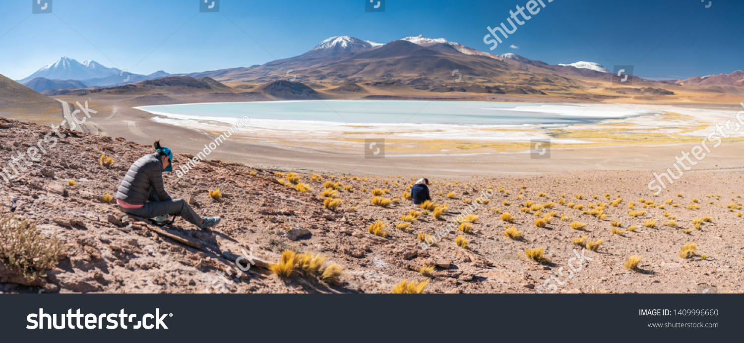 Two women outdoor photographers taking photos at Tuyajto Lagoon, awe turquoise color at Atacama Desert. An arid landscape full of salt flats and lakes with beautiful volcanic scenery on a sunny day #1409996660