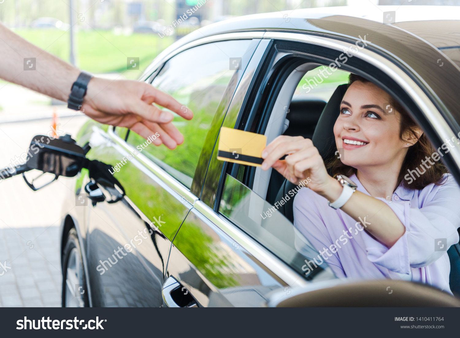 selective focus of happy woman sitting in car and giving credit card to worker at gas station  #1410411764