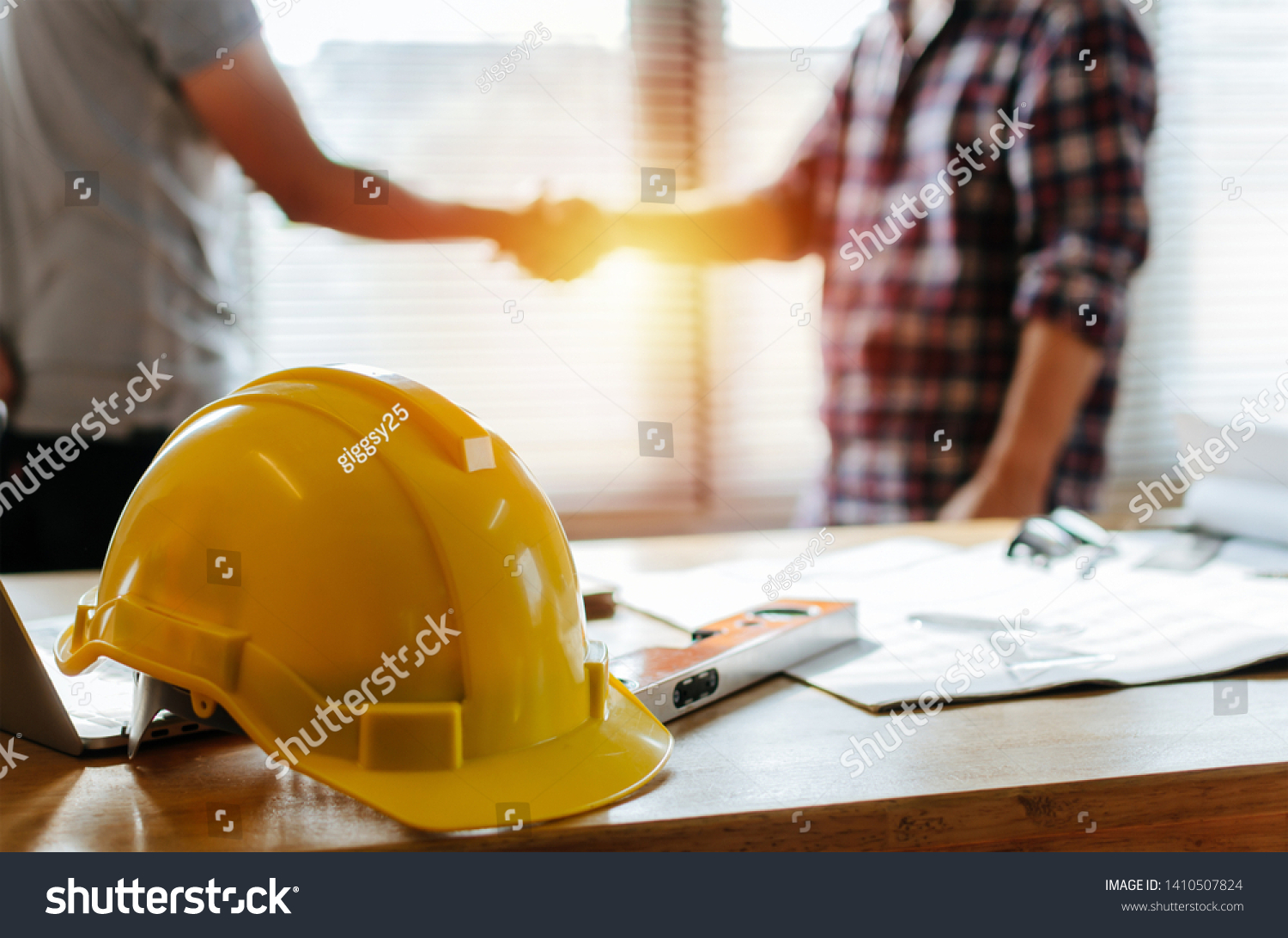 yellow safety helmet on workplace desk with construction worker team hands shaking greeting start up plan new project contract in office center at construction site, partnership and contractor concept #1410507824