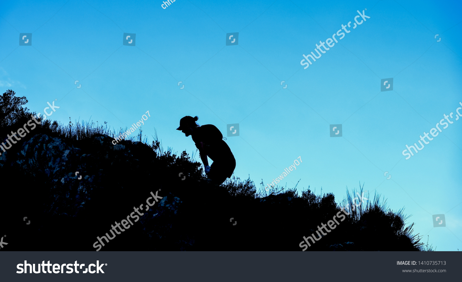 Dramatic silhouette of a person hiking and climbing a steep mountain #1410735713