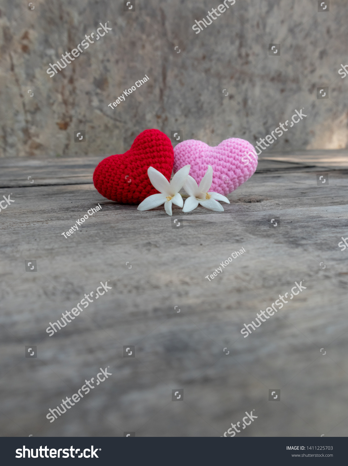 Knitting red and pink hearts with white Millingtonia on the rough wooden table. The background of rock wall with sun light. Copy space for editing #1411225703