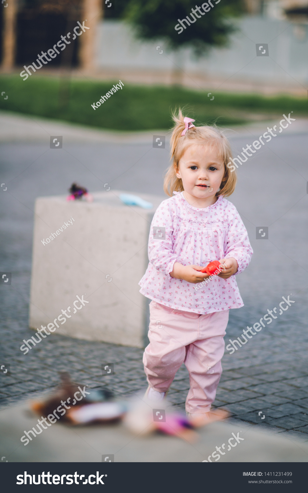 A little pretty little girl in pink pants plays on the waterfront of the lake #1411231499