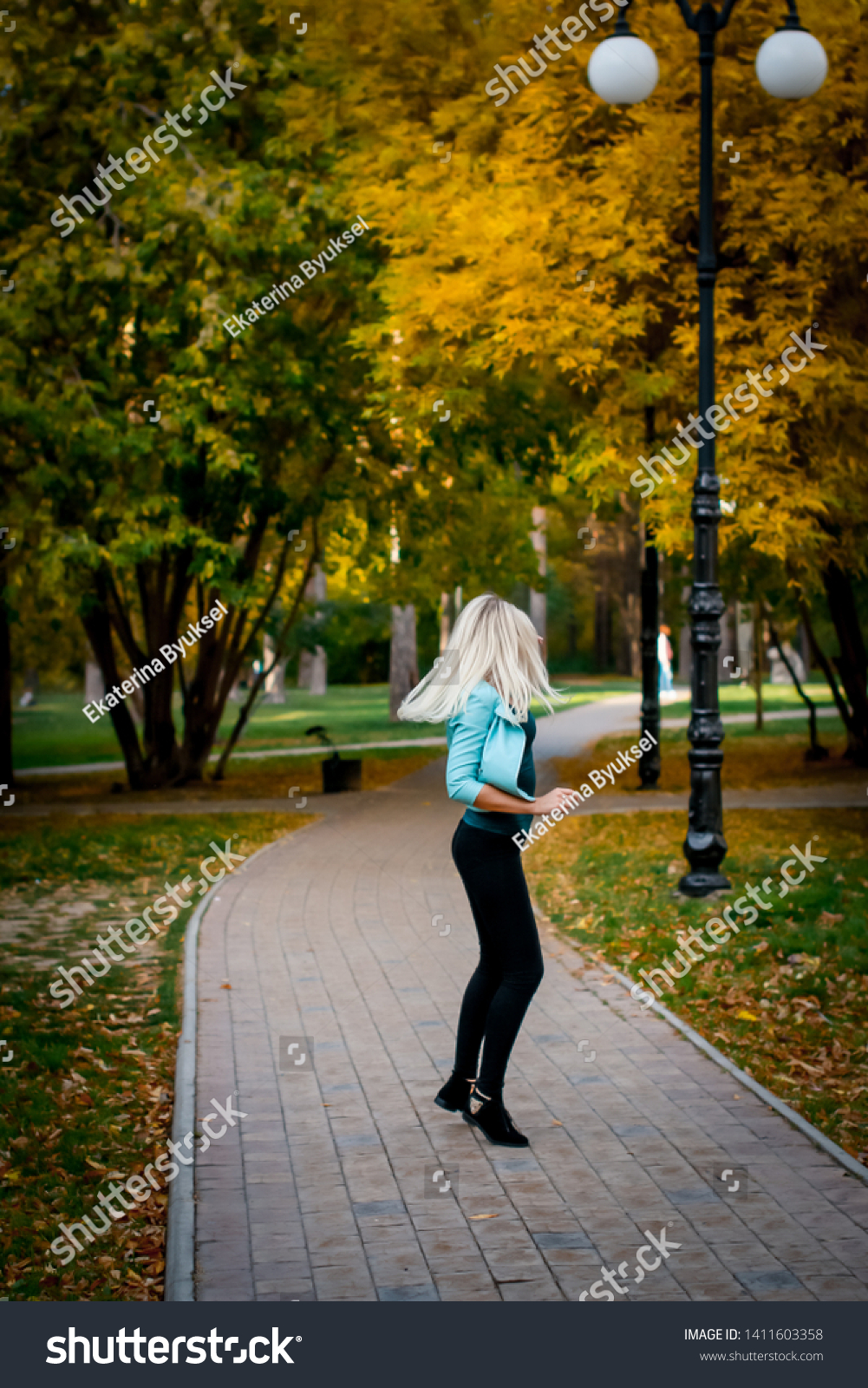 Portrait of a beautiful young woman enjoying autumn in the park. Attractive blonde in the park in autumn against a background of trees with yellow foliage. Sunset photography of the elephant #1411603358