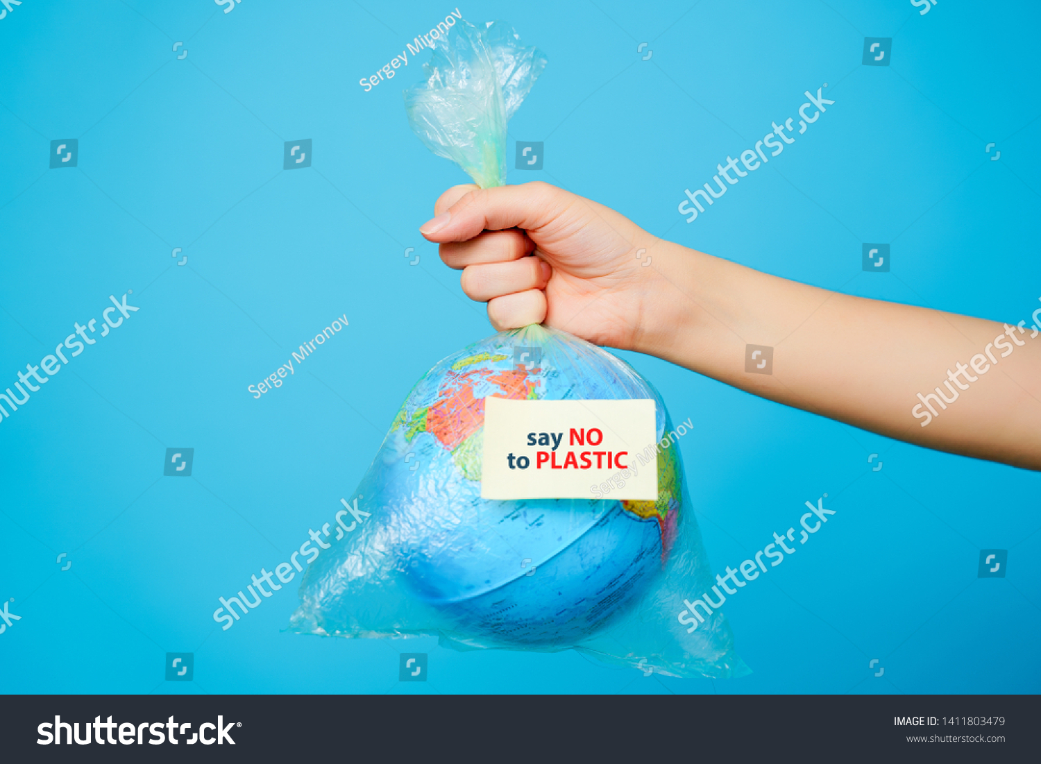 Woman holds in hands plastic bag and planet earth with text sticker-SAY NO TO PLASTIC at blue background. The concept of plastic pollution. #1411803479