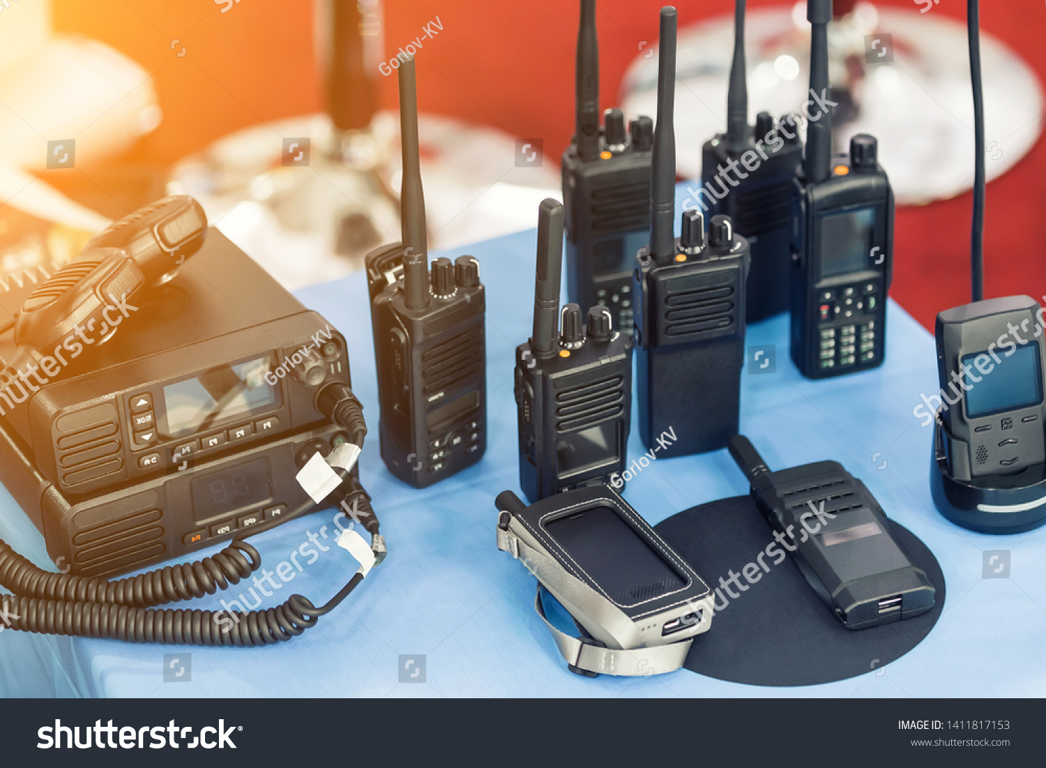 Many portable radio transceivers on table at technology exhibition. Different walkie-talkie radio set. Communication devices choice for military and civil use #1411817153