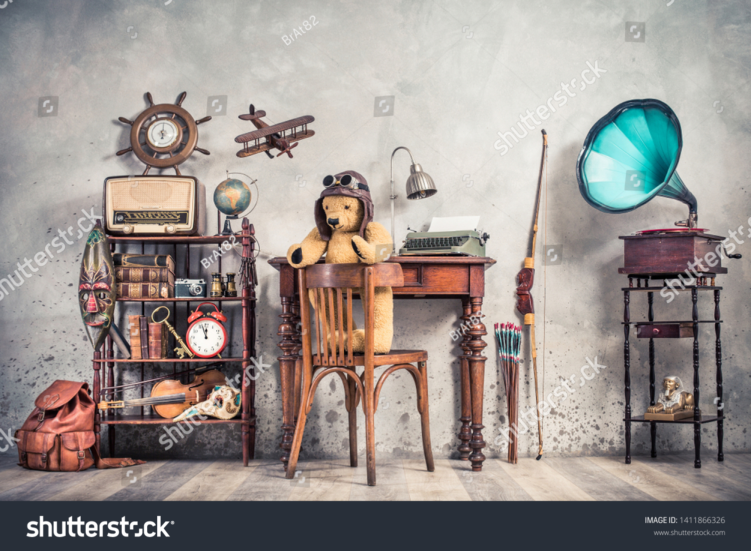 Teddy Bear toy on chair, typewriter, vintage gramophone, old books, radio, globe, binoculars, carnival mask, camera, fiddle on shelf, steering wheel, plane, travel backpack, bow. Retro style photo #1411866326