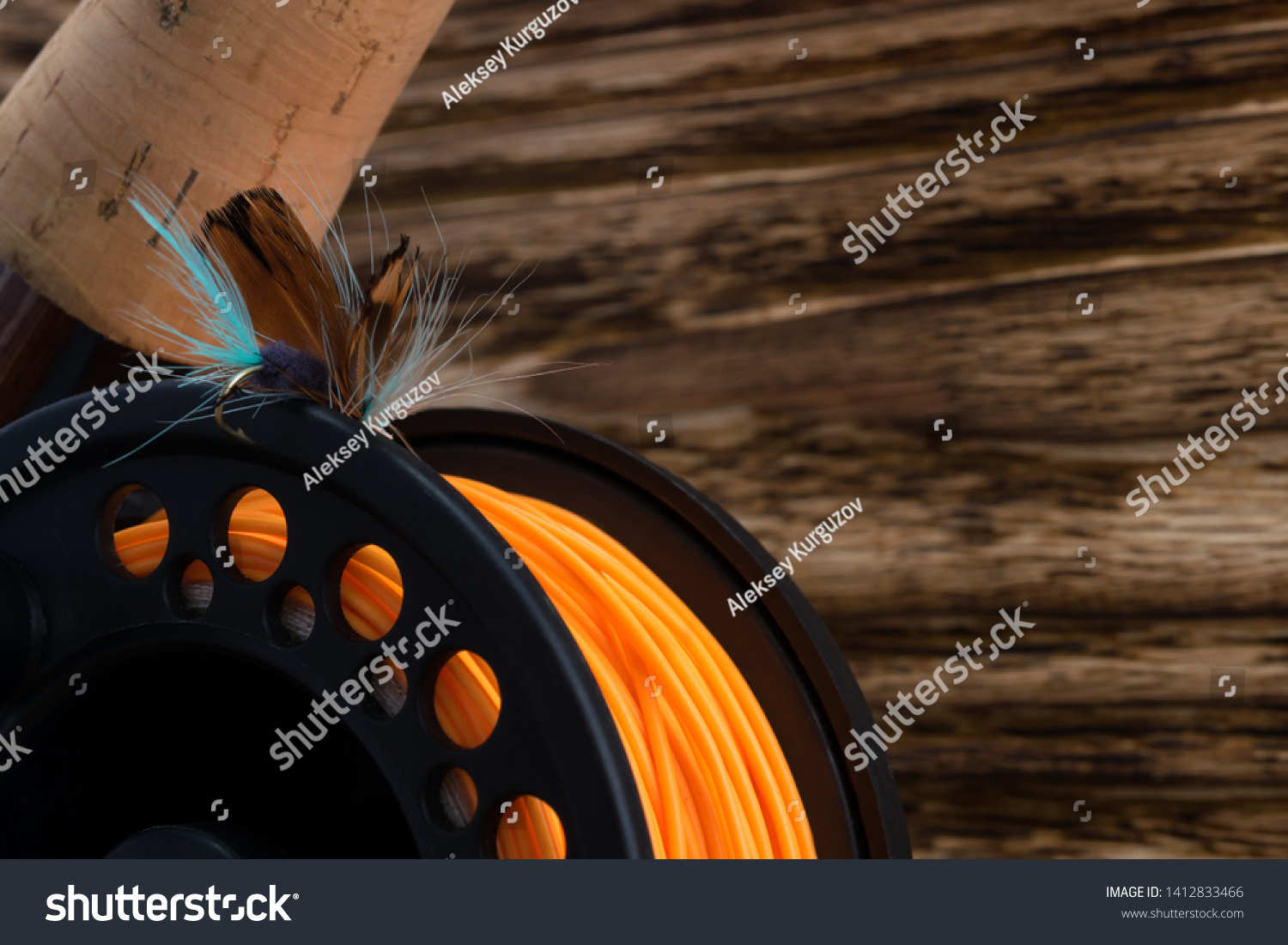 reel with orange fishing line and feather bait lie on a wooden background #1412833466