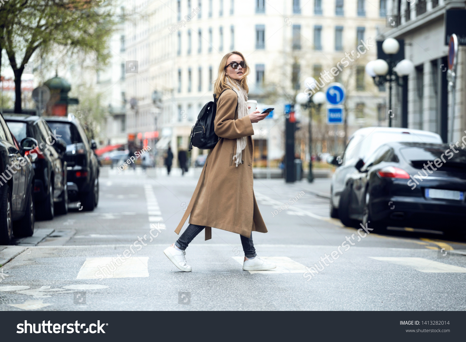 Shot of pretty young woman crossing the street while holding the smartphone and looking sideways. #1413282014